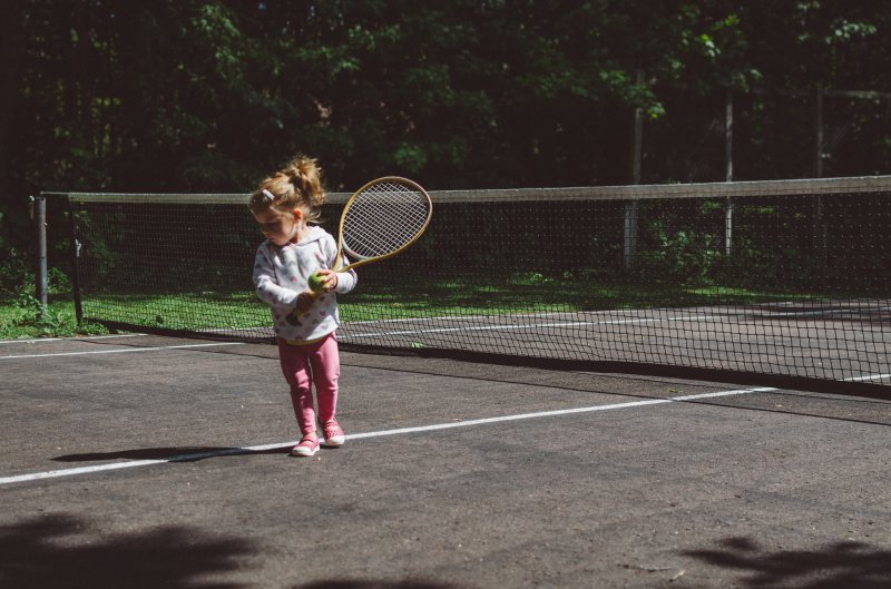 Kleines Mädchen mit einem Tennisschläger an einem Netz