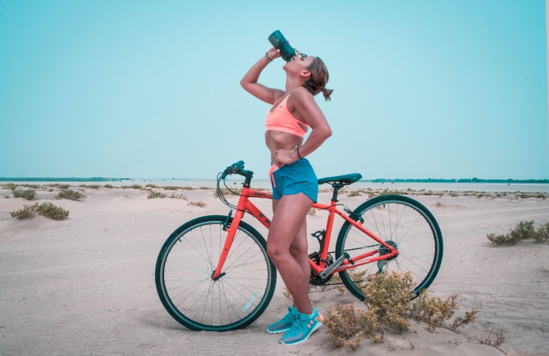 Eine Frau steht neben einem Fahrrad und trinkt etwas aus einer Flasche