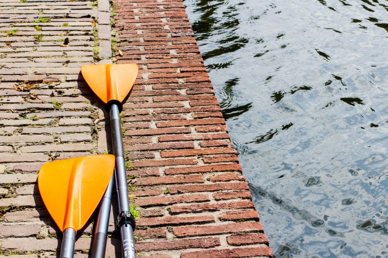 Orange Paddel für ein Kinderschlauchboot liegen am Boden neben einem Gewässer