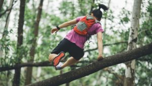 Trailrunner mit Rucksack springt über Baumstamm