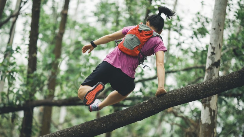 Trailrunner mit Rucksack springt über Baumstamm