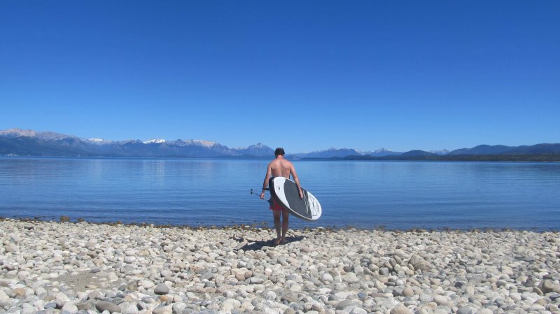 SUP-Boarder steht an einem See vor einer Bergkulisse