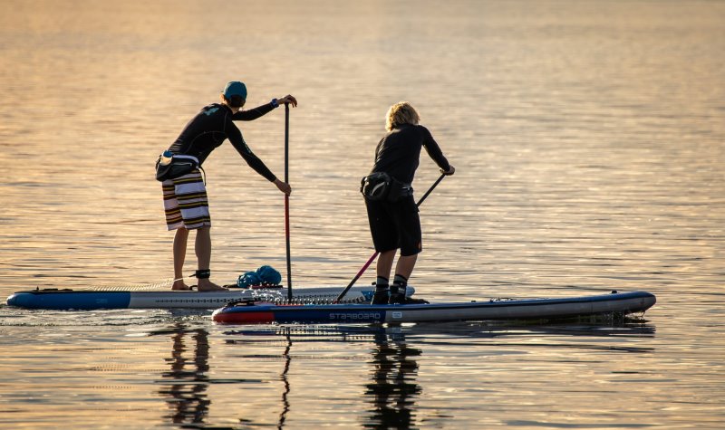 Zwei Personen betreiben Stand-Up-Paddling auf dem Meer bei Sonnenuntergang und tragen dabei SUP Socken.