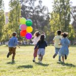 Kinder rennen mit bunten Luftballons auf einer Wiese