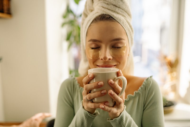 Frau mit einer Gesichtsmaske und einem Handtuchturban trinkt einen Tee.